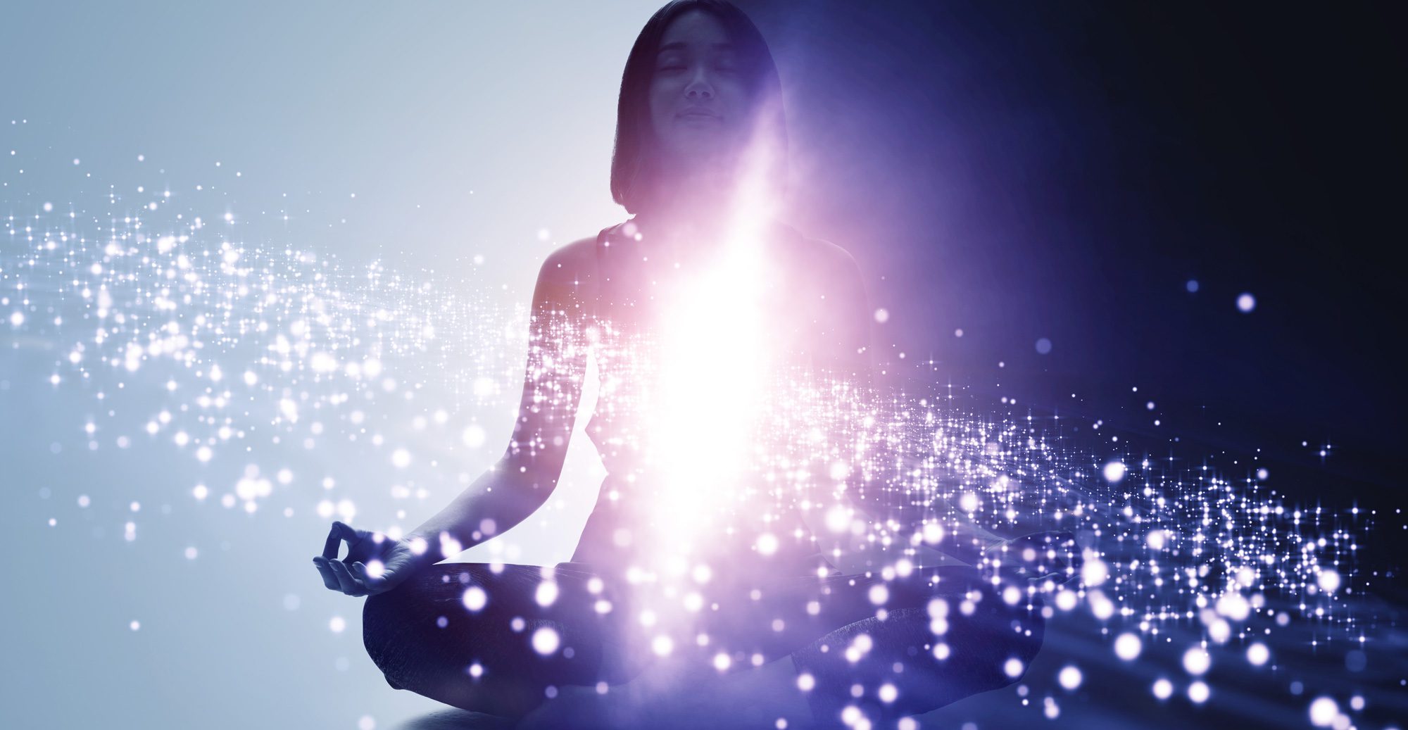  A person is sitting in a meditative pose with their eyes closed while sparkles of light surround them.